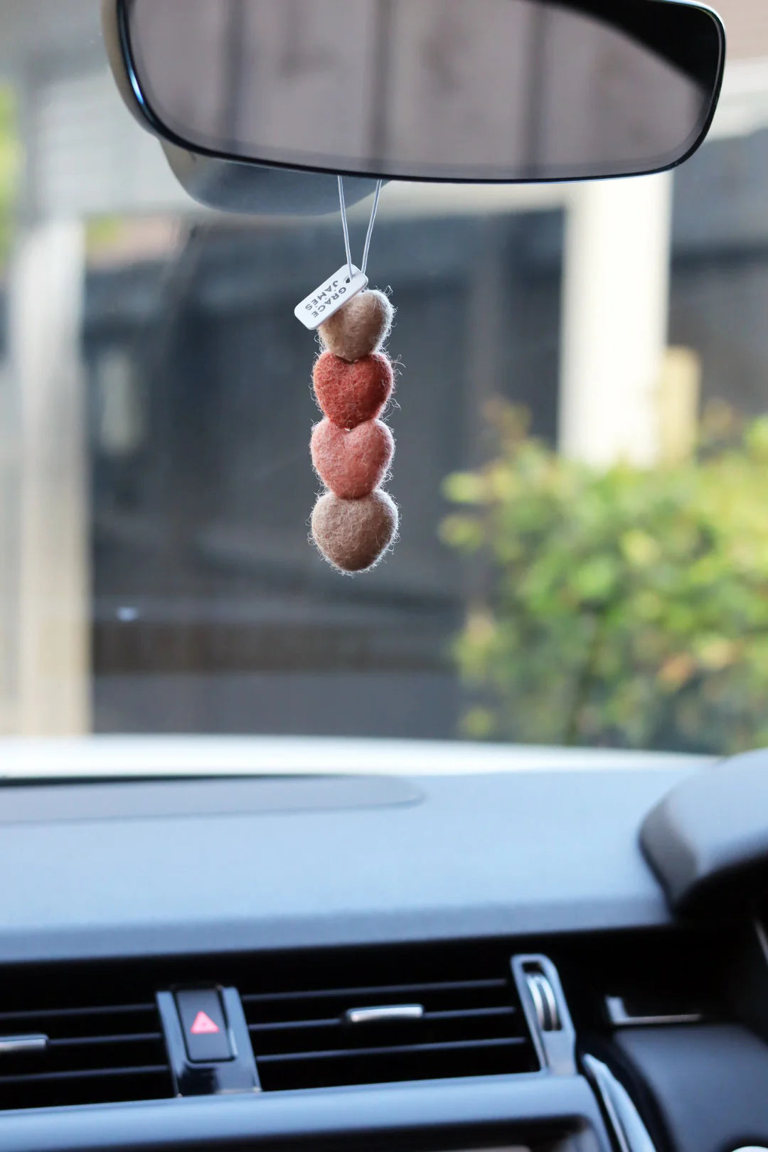 Felt shaped hearts on string car air freshener hanging from a car's rearview mirror with a blurred background