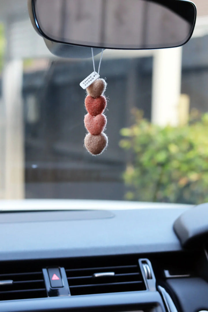 Felt shaped hearts on string car air freshener hanging from a car's rearview mirror with a blurred background