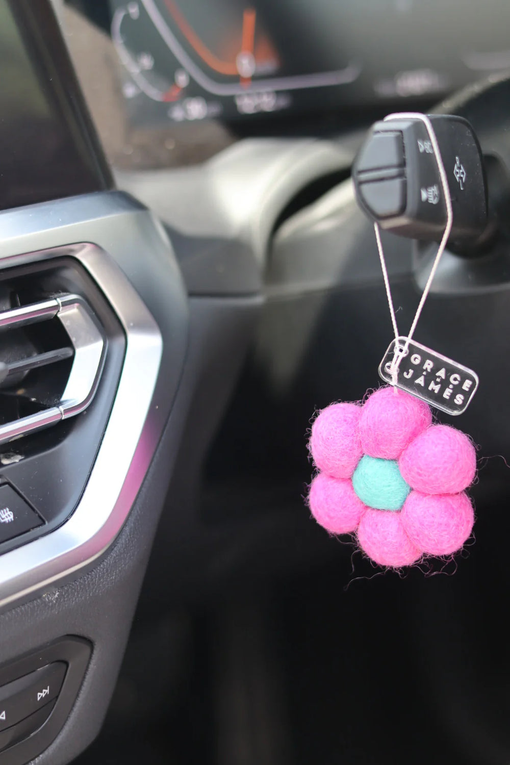 Pink flower-shaped car air freshener with a tag on a car dashboard.