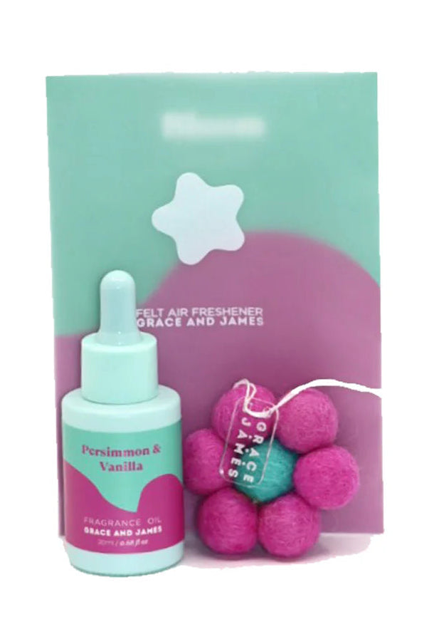 Fragranced oil bottle with packaging and pink flower shaped air freshener on a white background