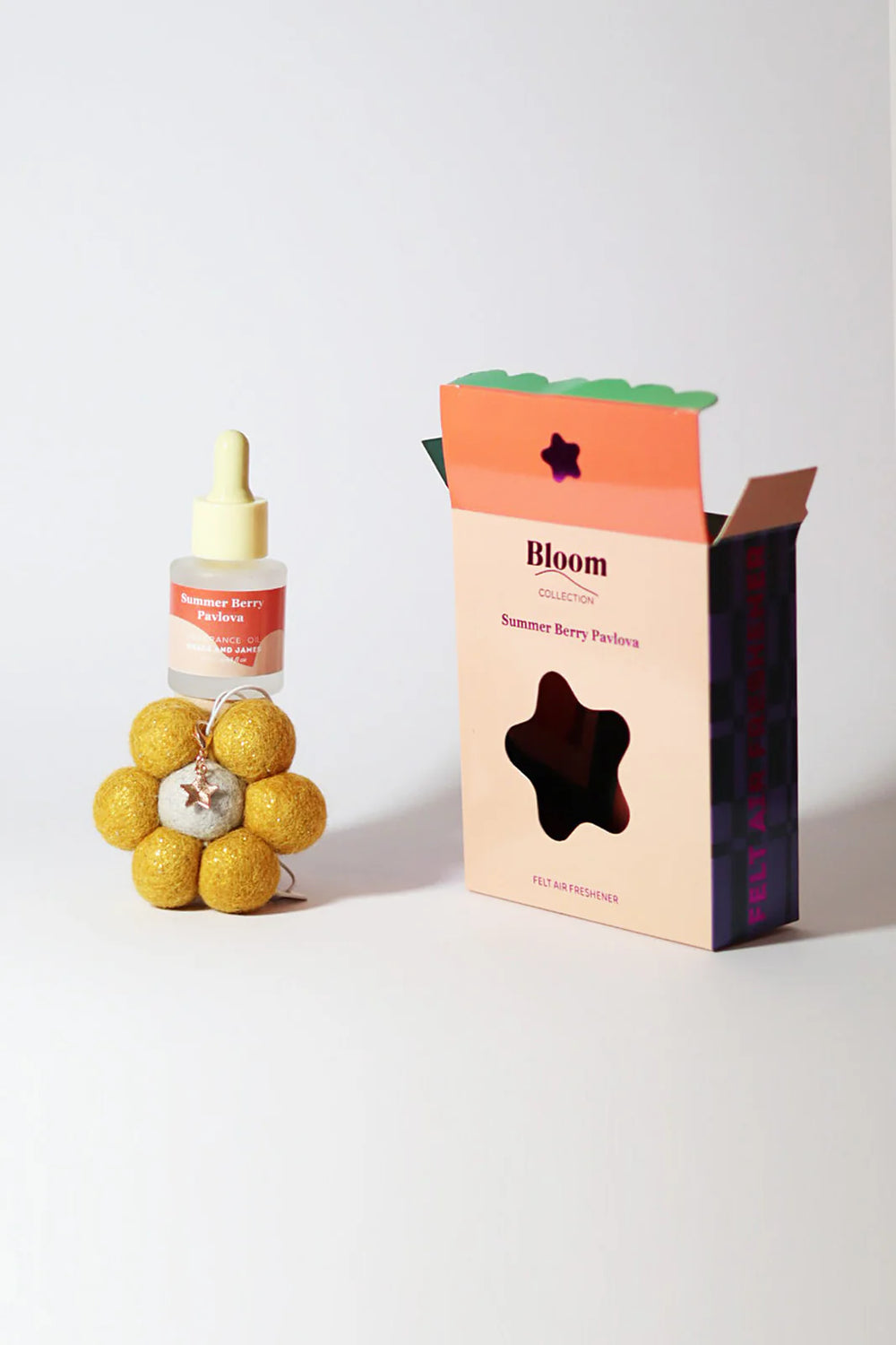 Bloom product packaging with a fragranced oil dropper bottle and flower shaped felt air freshener and charm on a light background