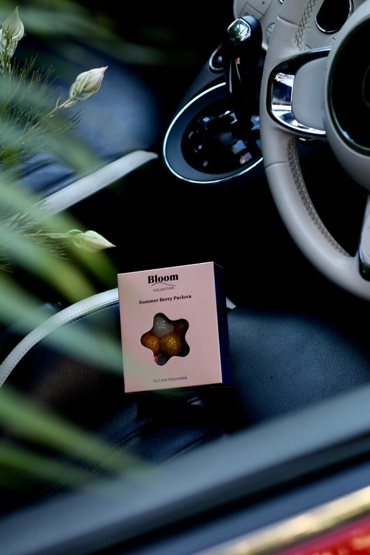 Pink packaging labeled 'Bloom' in a car's cup holder with steering wheel and dashboard in the background.