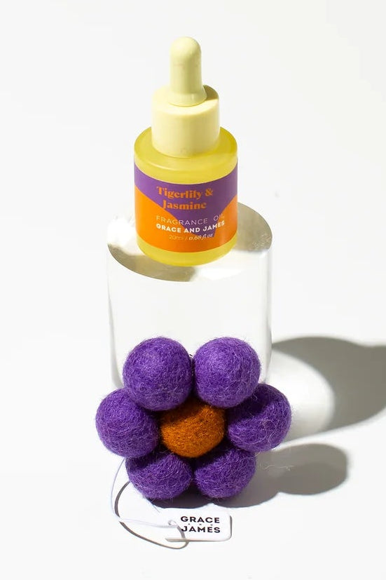 Fragranced oil bottle with purple flower-shaped felt air freshener on a white background