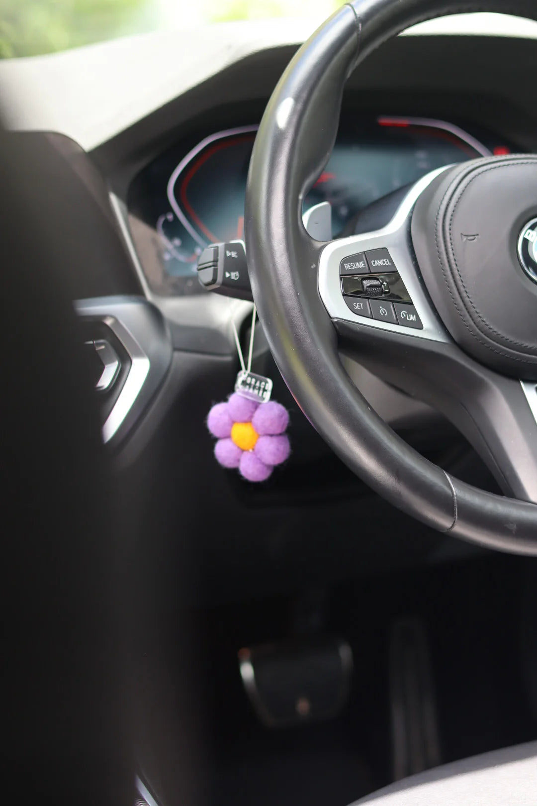 Car interior with a purple flower-shaped car air freshener hanging from the steering wheel.