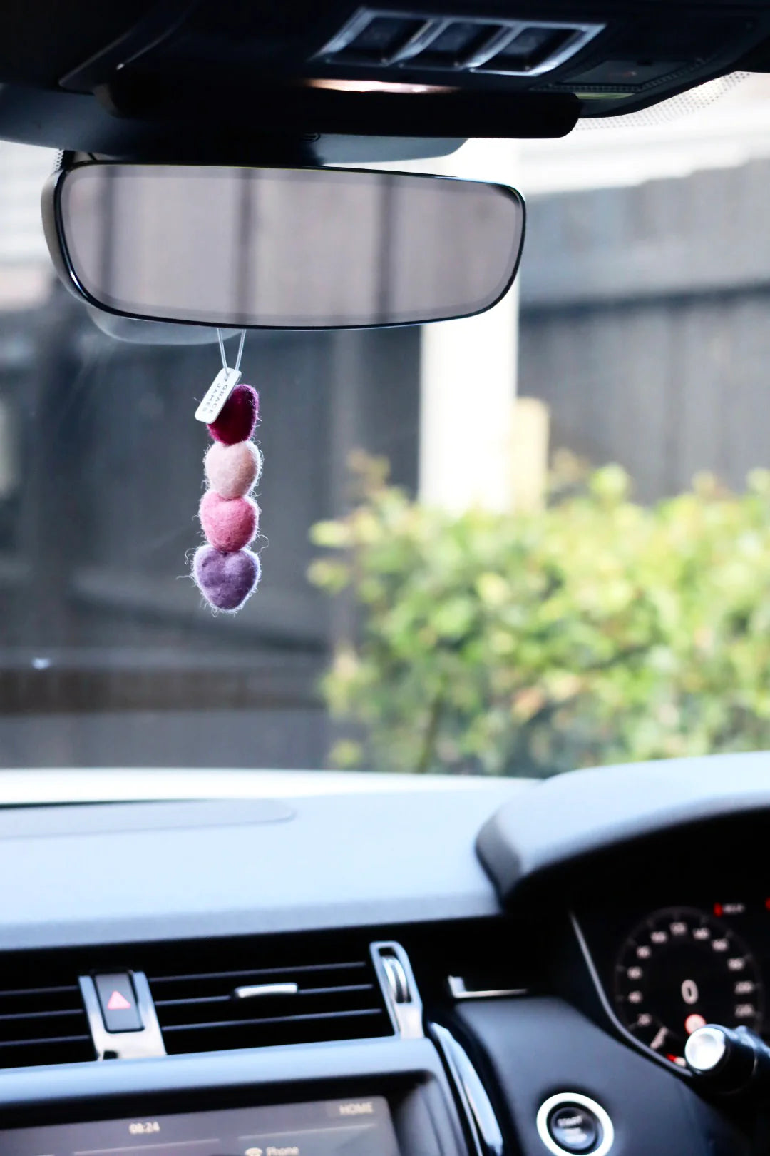 Car heart shaped felt air freshener hanging from the rearview mirror with a blurred outdoor background