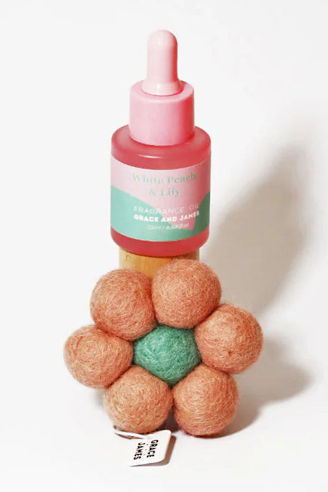 Fragranced oil bottle with pink cap and flower shaped felt air freshener on a white background