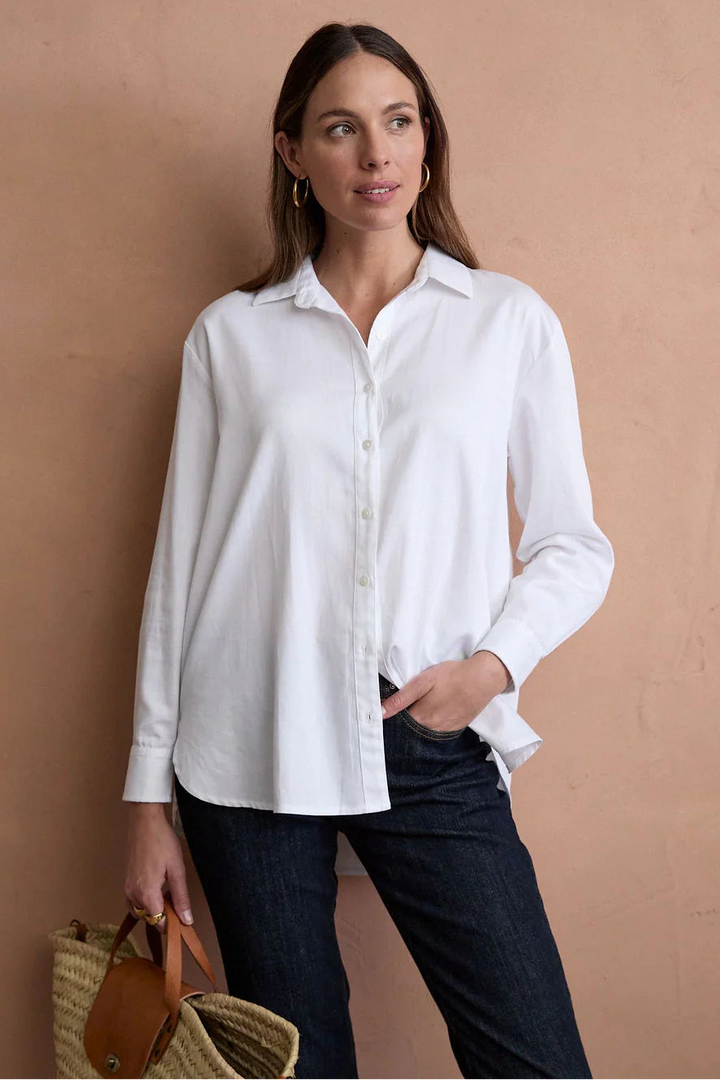 Woman wearing a white shirt and dark pants against a beige wall