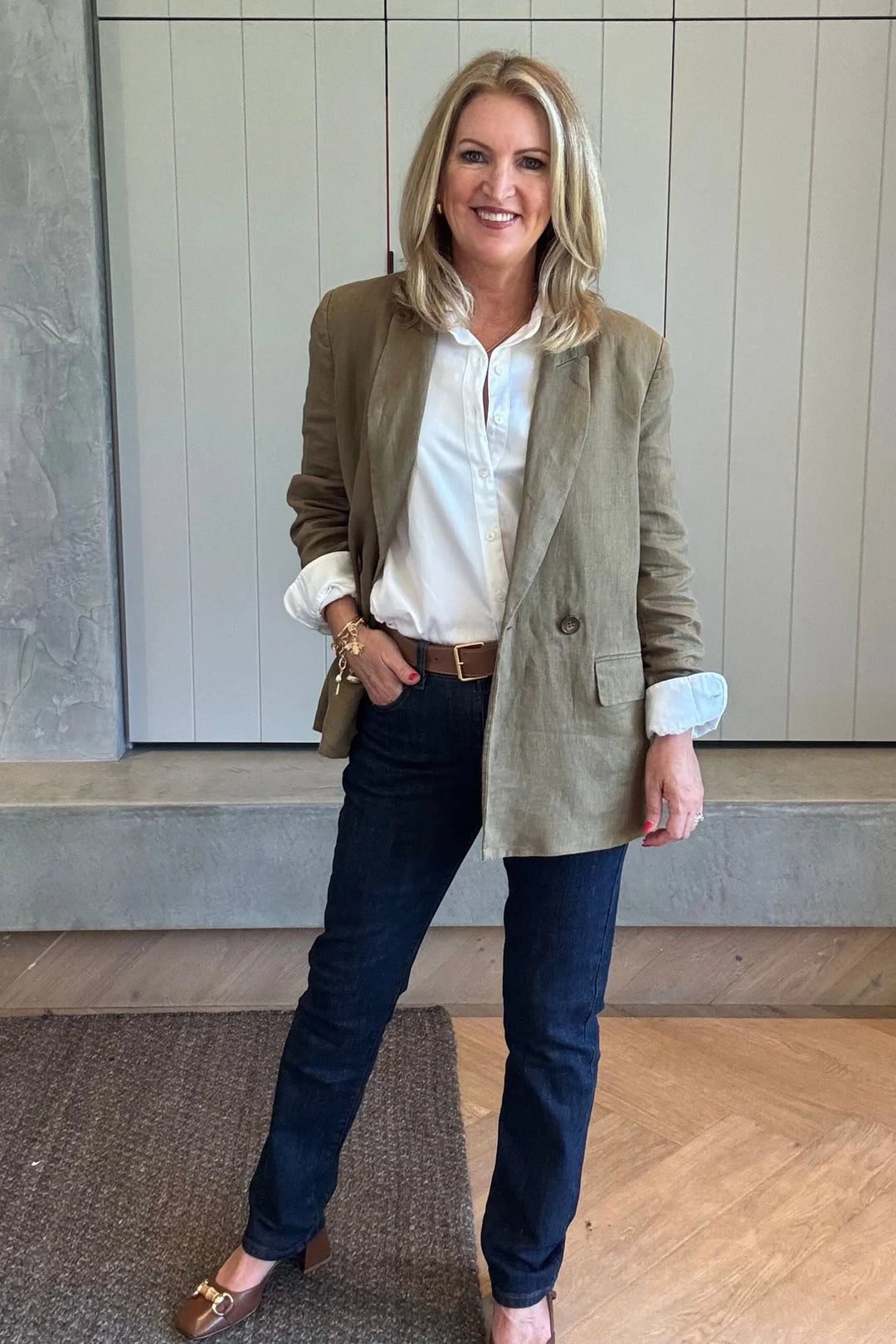 Woman wearing a green blazer, white shirt, and dark jeans indoors.