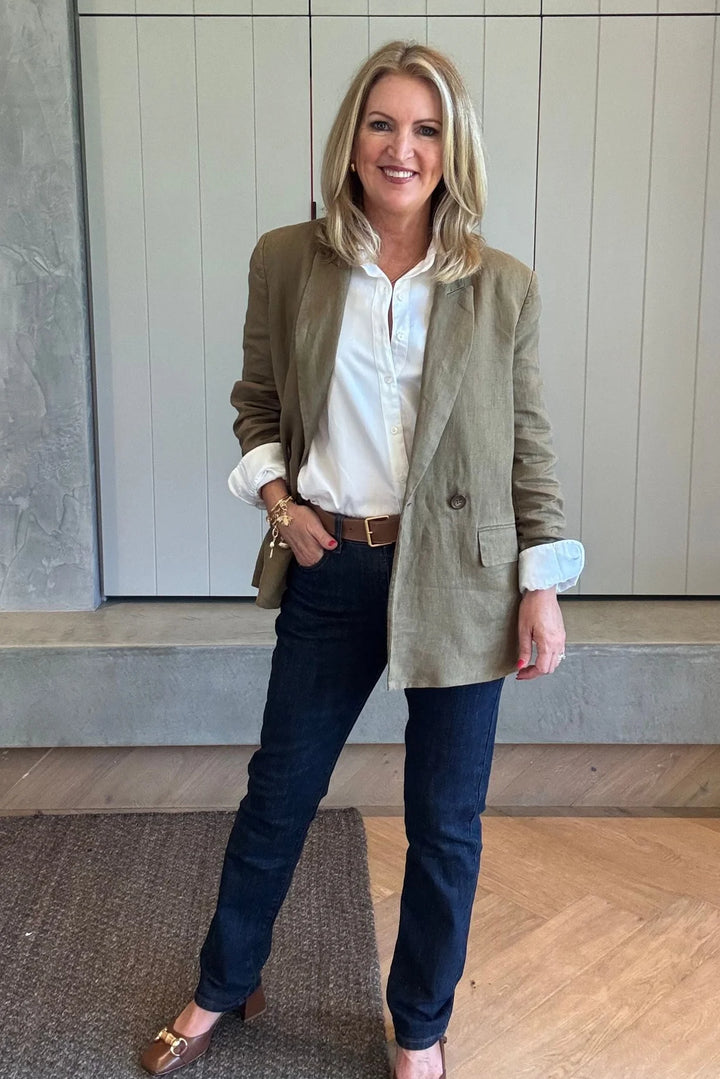 Woman wearing a green blazer, white shirt, and dark jeans indoors.