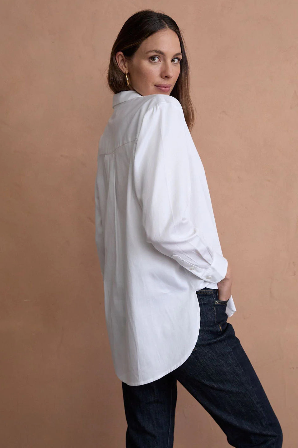 Woman wearing a white shirt and dark jeans against a beige background