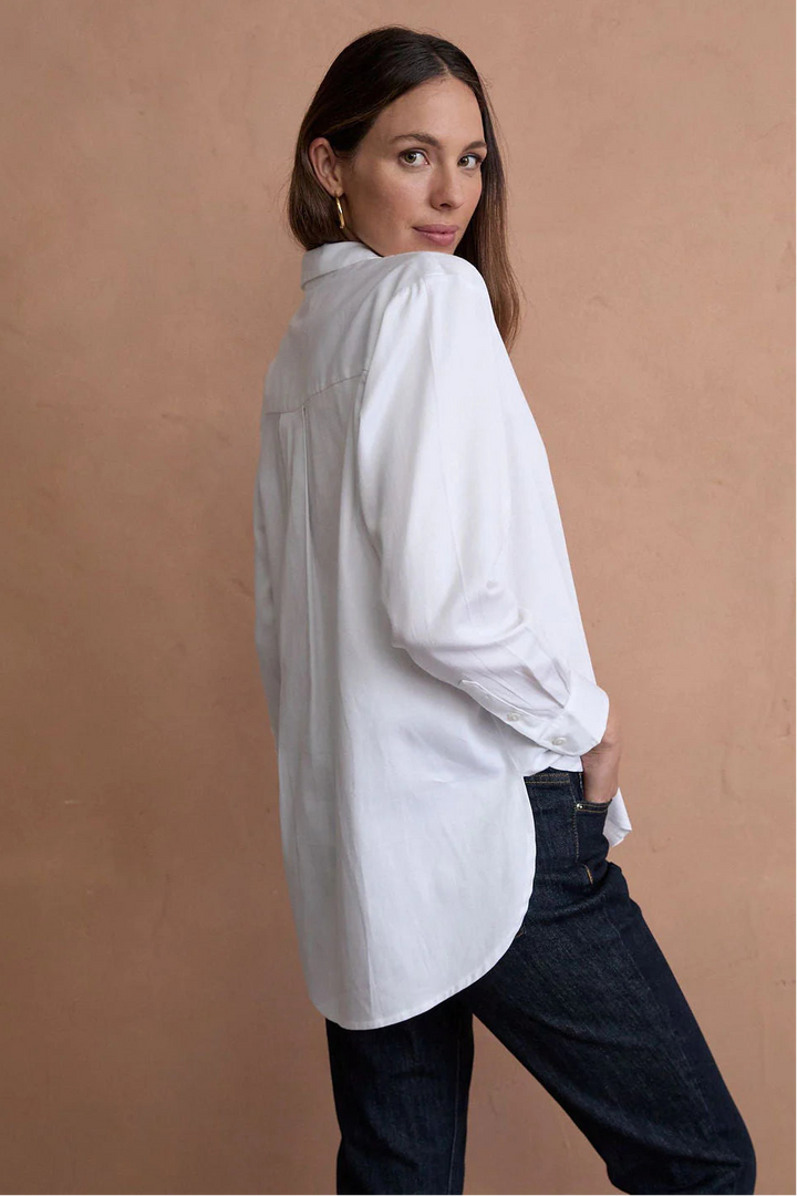 Woman wearing a white shirt and dark jeans against a beige background