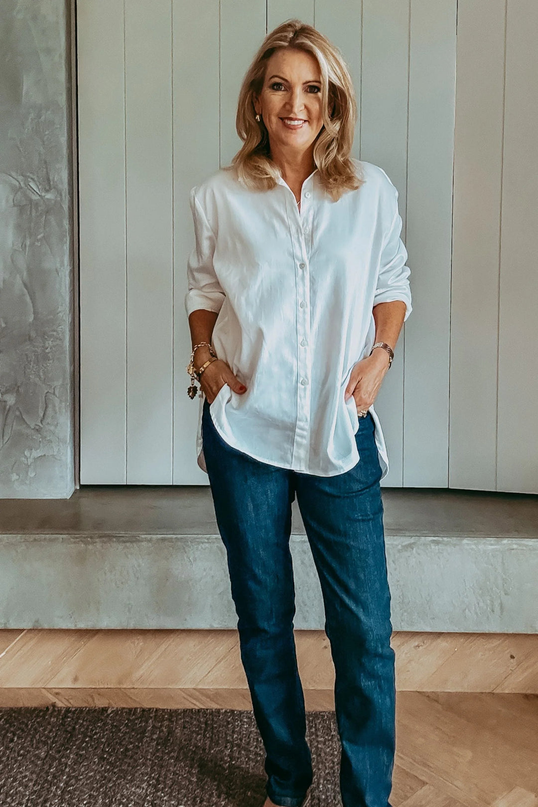 Woman wearing a white shirt and blue jeans standing indoors.