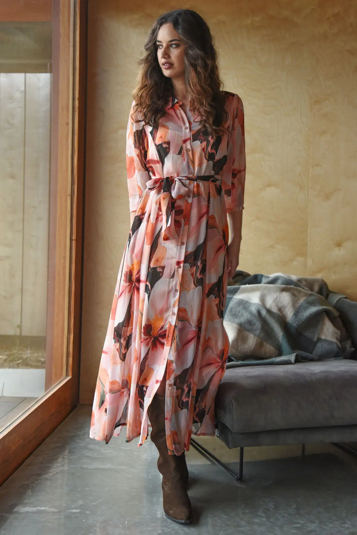 Woman wearing a long floral dress in a room with a couch and mirror.