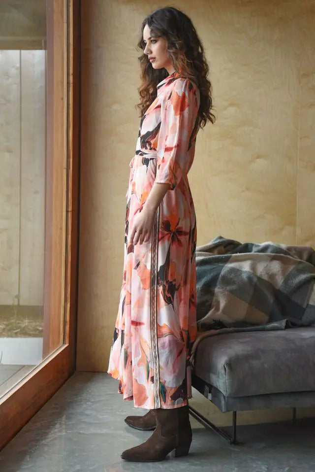 Woman in a floral dress standing in a room with a couch and window.