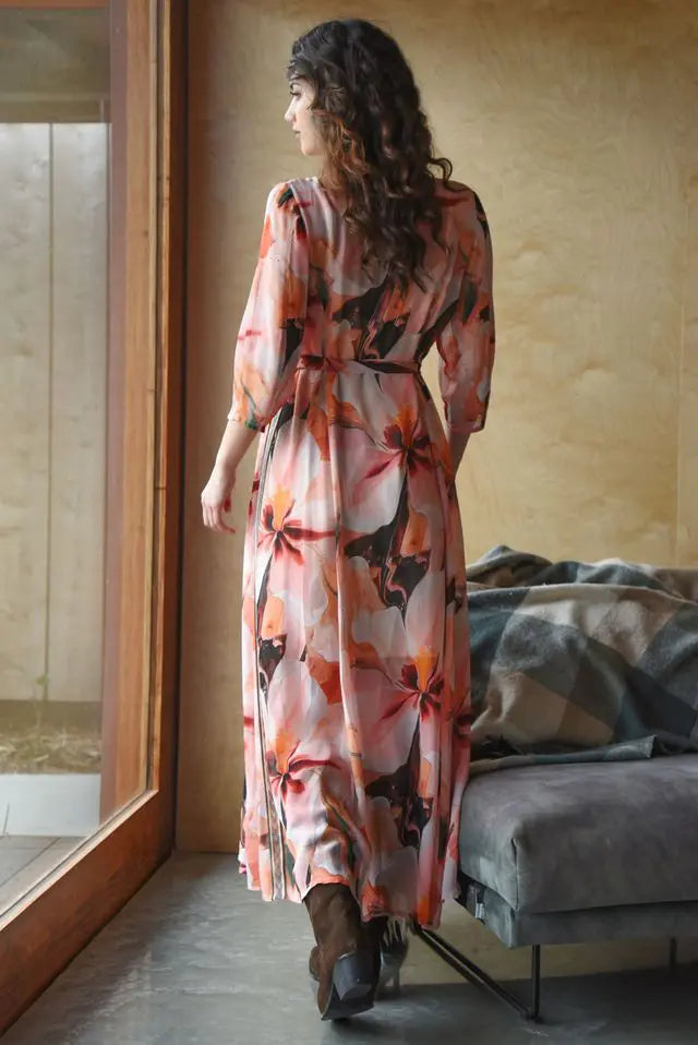 Woman in a floral dress standing by a window in a room with a couch.
