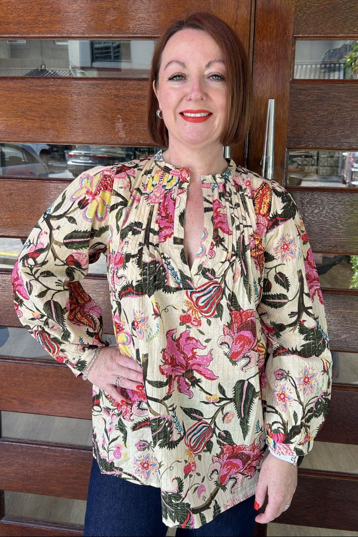 Woman wearing a floral blouse standing in front of a wooden door.