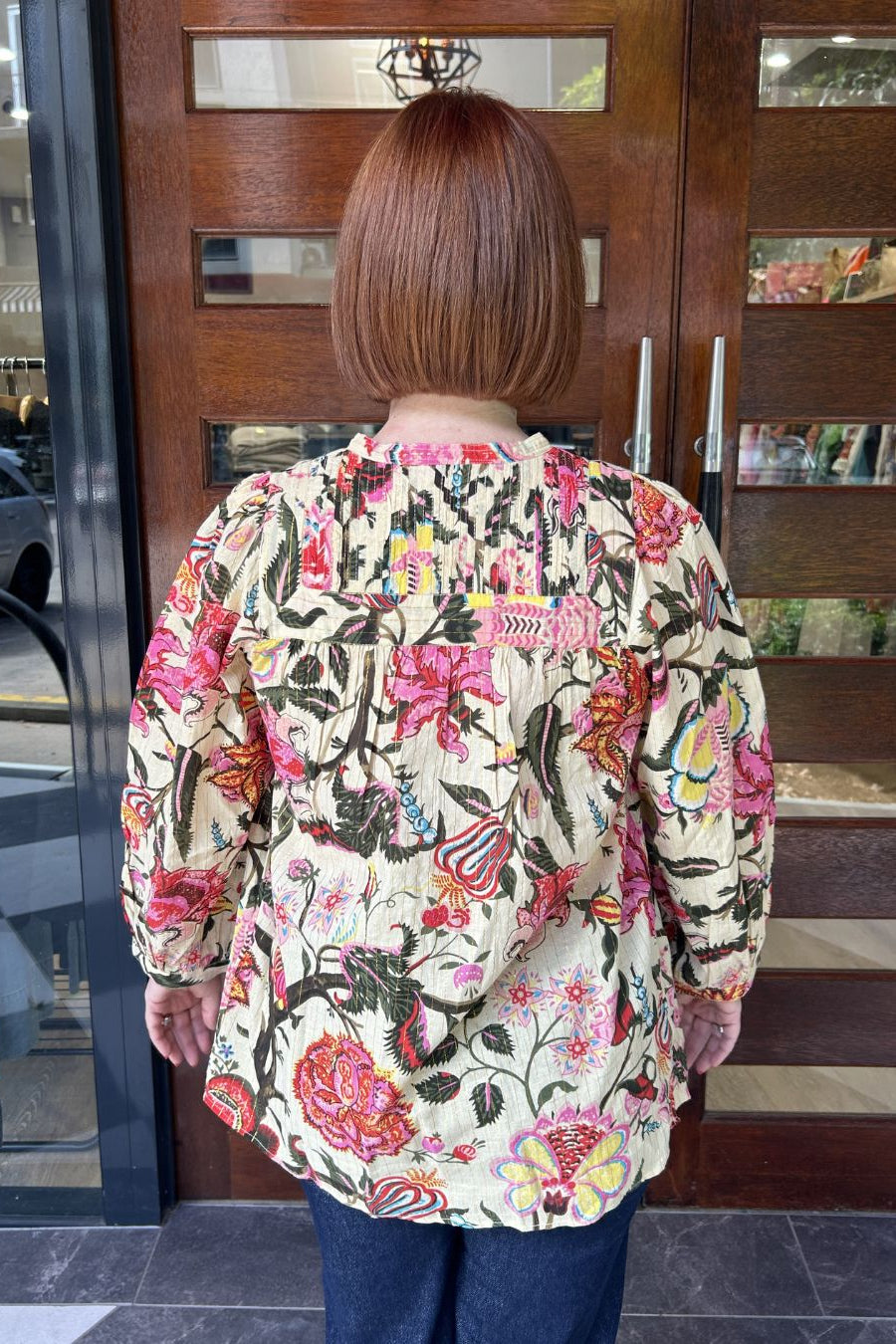 Person wearing a colorful floral blouse standing in front of a wooden door.