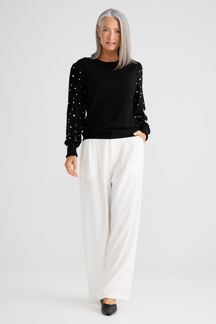 Woman wearing a black sweater with white polka dots and white pants on a white background