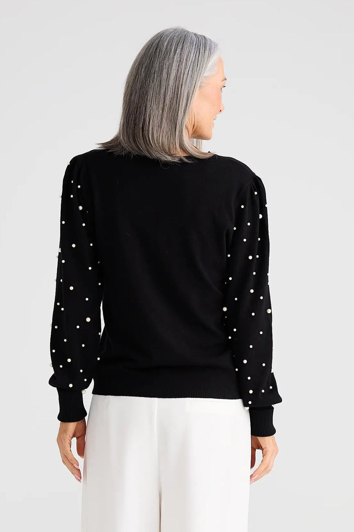 Person wearing a black top with white embellishments and white pants on a white background
