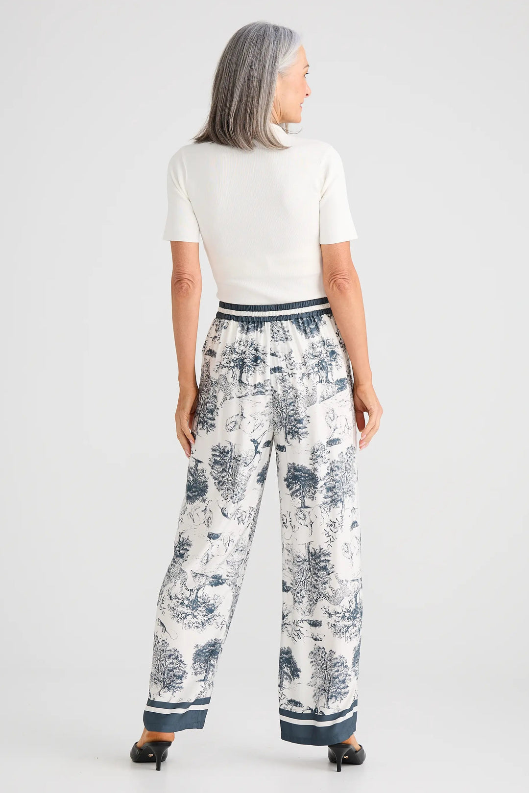 Woman wearing a white top and patterned pants on a plain background