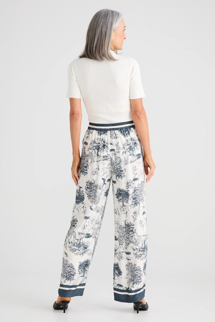 Woman wearing a white top and patterned pants on a plain background