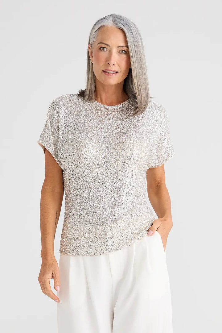 Woman wearing a patterned top and white pants on a white background