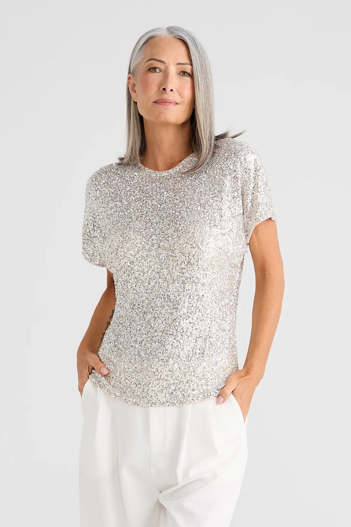 Woman wearing a light gray sleeveless top and white pants on a white background