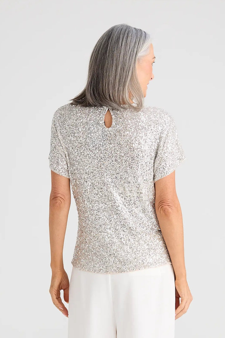 Person wearing a light gray patterned top and white pants on a white background