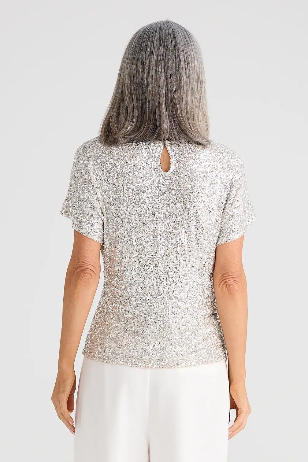 Person wearing a light-colored top and white pants on a plain background