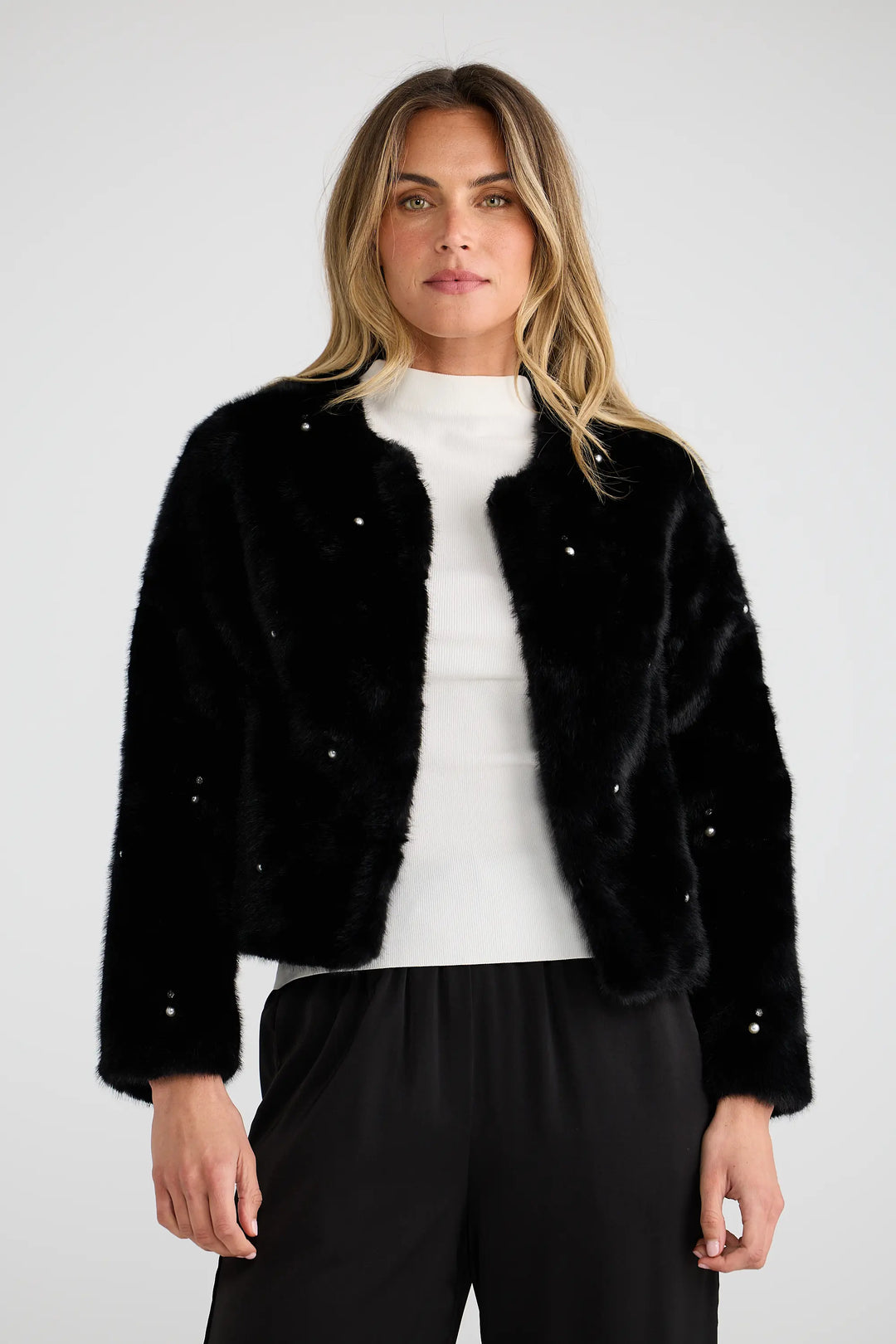 Woman wearing a black faux fur jacket with white polka dots on a white background