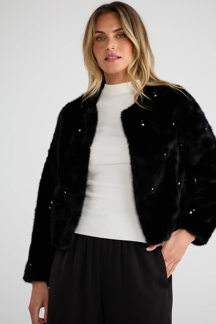Woman wearing a black embellished jacket over a white top and black pants on a light gray background