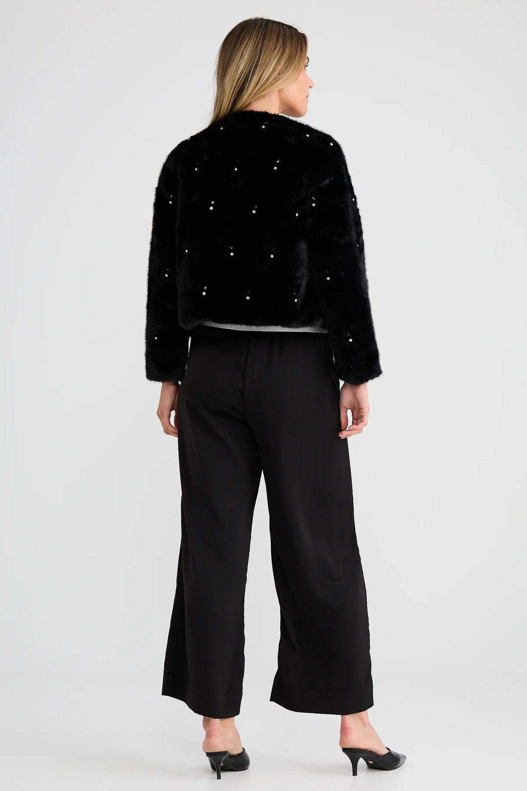 Woman wearing a black embellished jacket and black pants on a white background