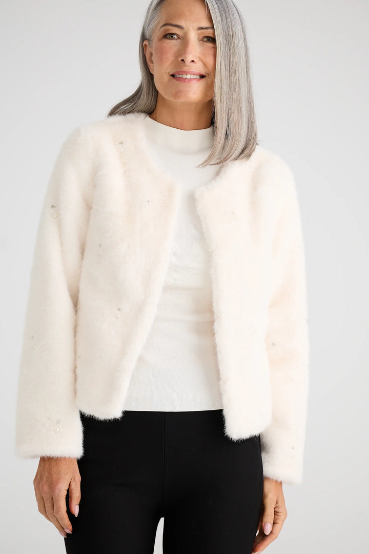 Woman wearing a cream-colored cardigan over a white top with black pants on a plain background