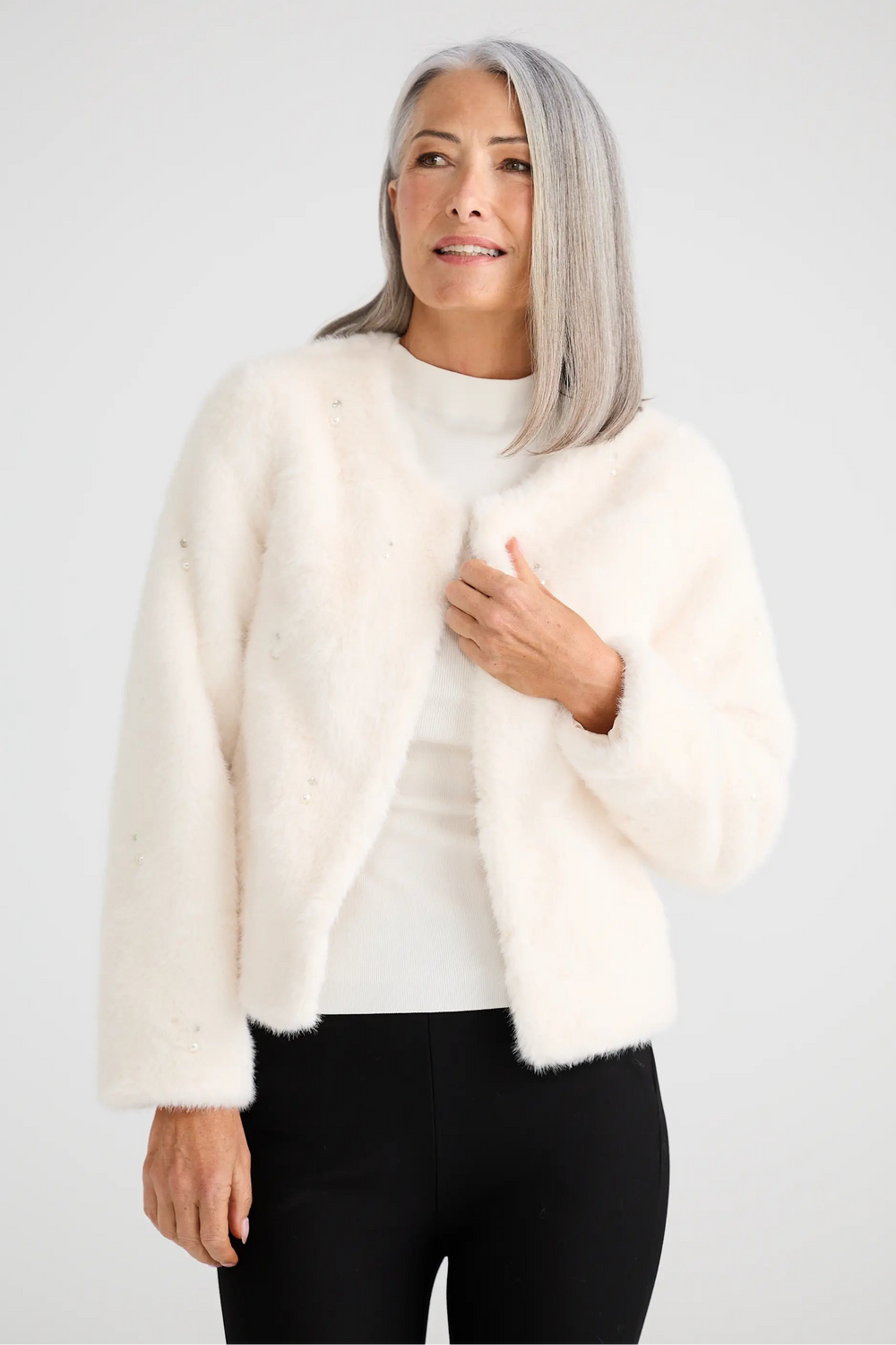 Woman wearing a white fur coat over a white sweater on a light gray background