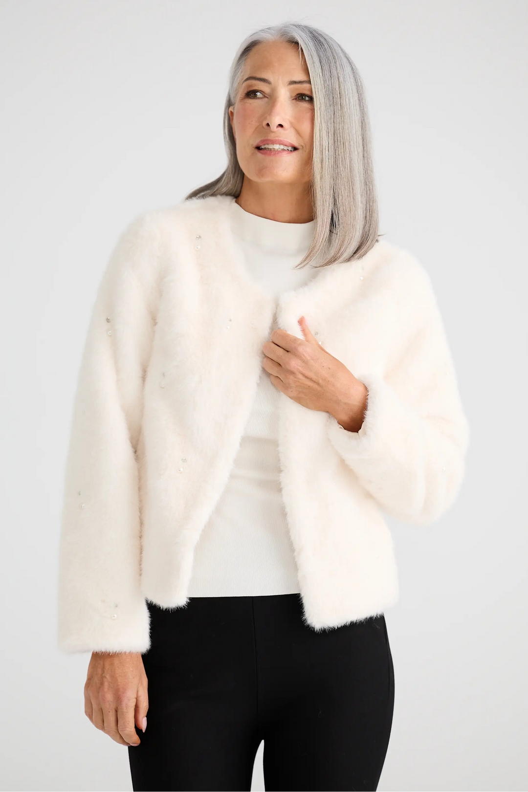 Woman wearing a white fur coat over a white sweater on a light gray background
