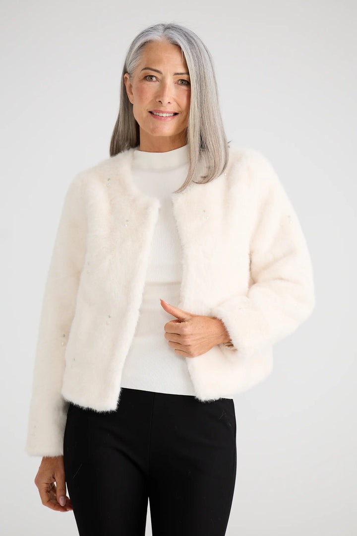 Woman wearing a cream fur coat over a white top and black pants on a white background