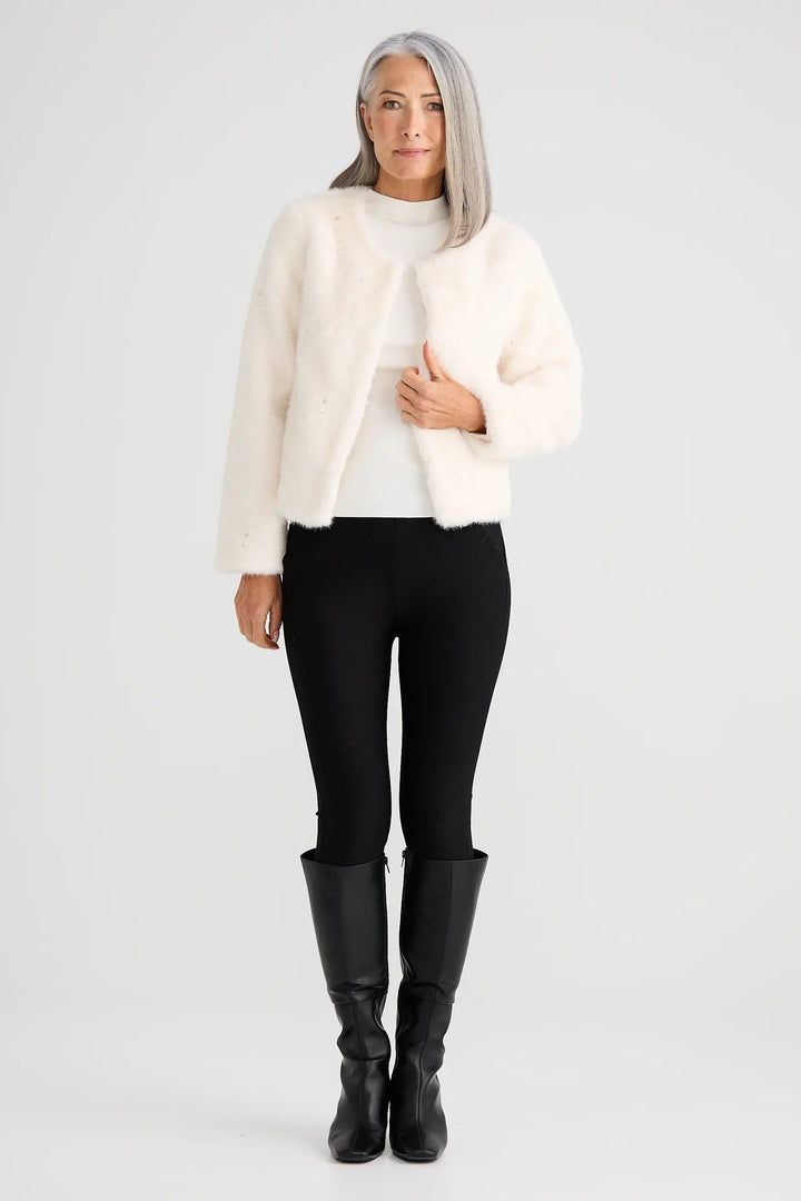 Person wearing a cream jacket, black pants, and black boots on a white background