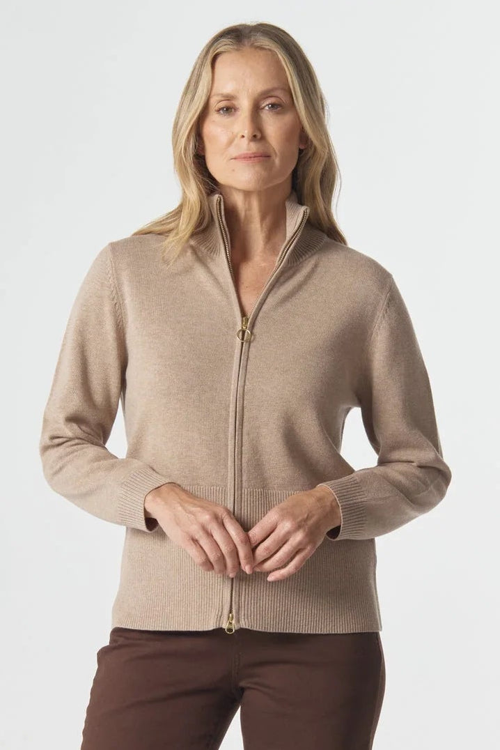 Woman wearing a beige zip-up sweater and brown pants on a white background