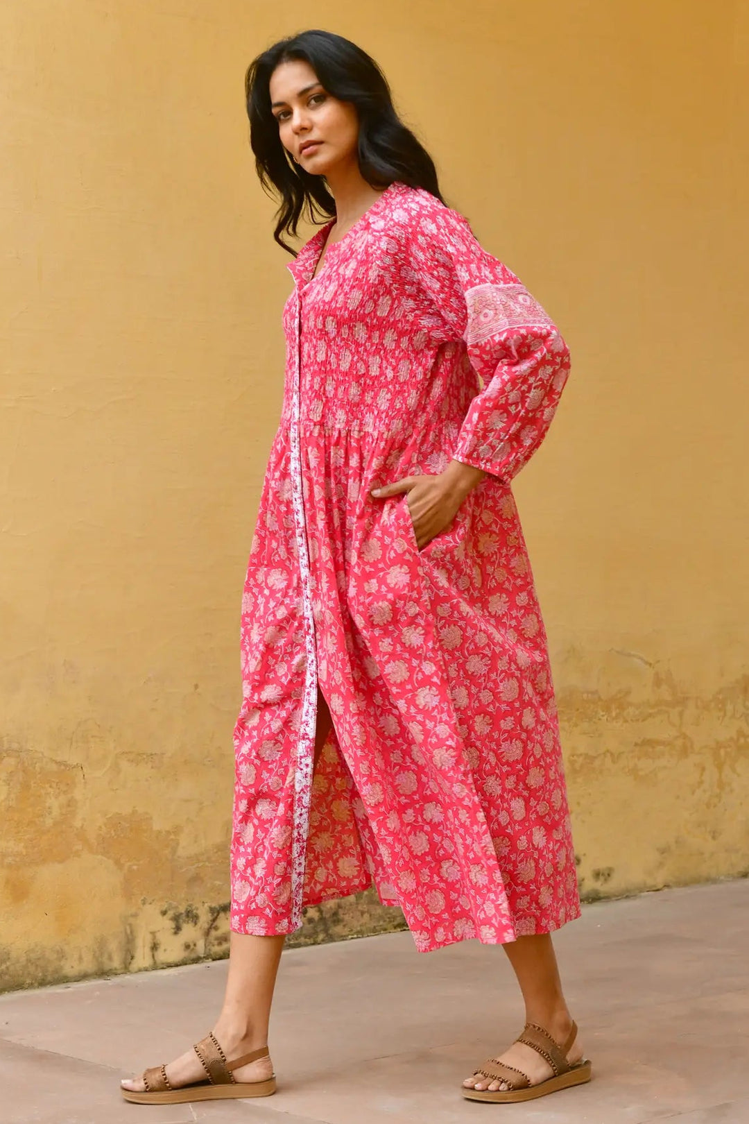 Woman wearing a pink patterned dress against a yellow wall. Azure & Indigo Camillia Maxi Dress Cherry