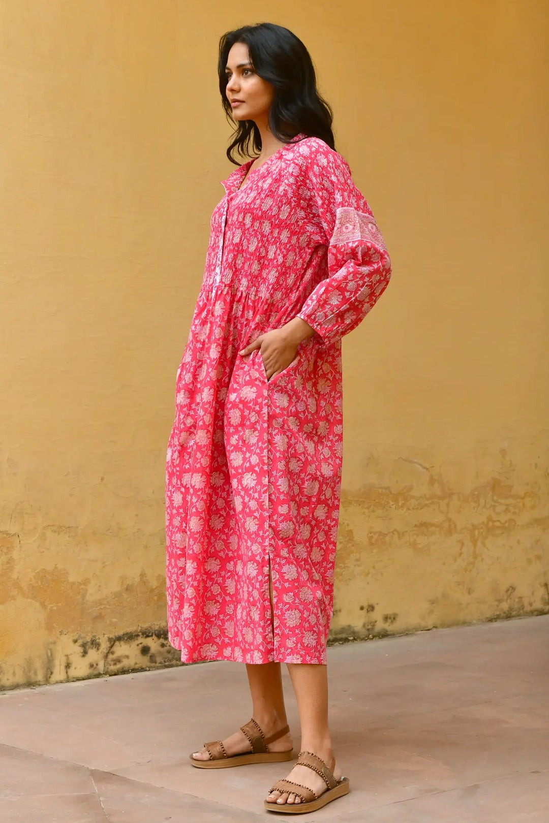 Woman wearing a pink floral dress against a yellow wall. Azure & Indigo Camillia Maxi Dress Cherry