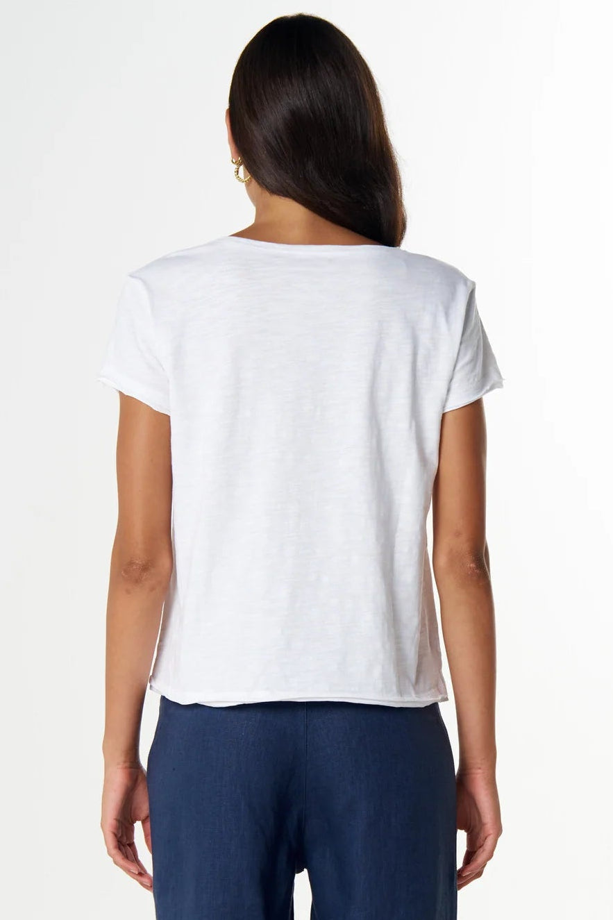 A woman viewed from behind wearing a white short-sleeve t-shirt and navy blue cropped pants, standing against a plain white studio background.