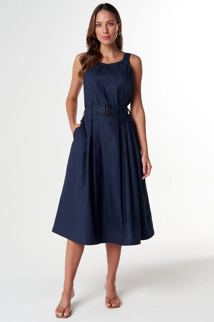 A woman modeling a sleeveless navy blue midi dress with a matching belt and buckle, standing against a plain white studio background.