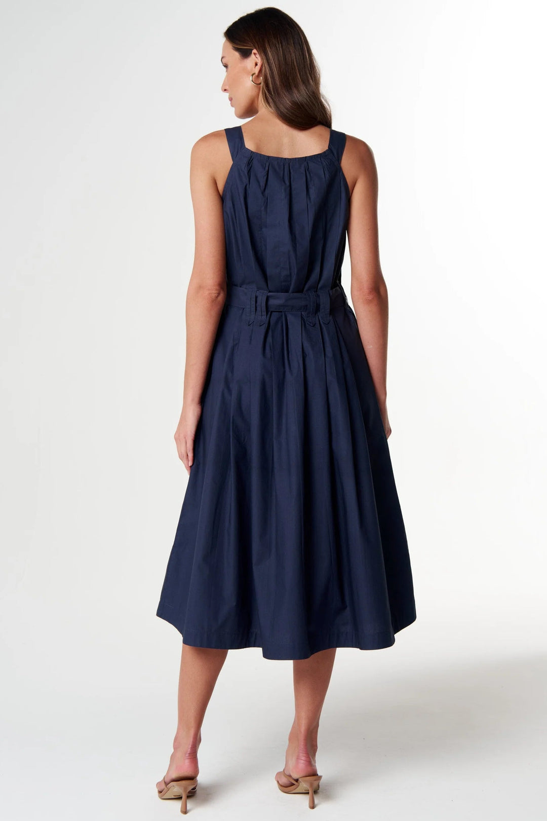 A woman modeling a sleeveless navy blue midi dress from the back, featuring a gathered bodice, a matching fabric tie belt at the waist, and a flared skirt, set against a plain white studio background.