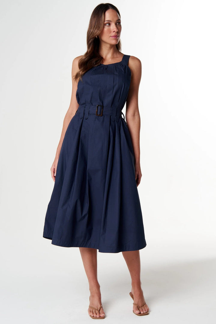 A woman modeling a sleeveless navy blue midi dress with a defined waist and belt, standing against a plain white studio background.