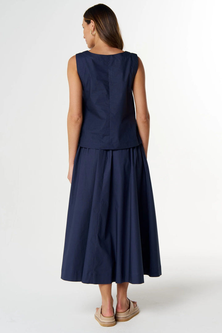 A woman viewed from the back wearing a sleeveless navy midi dress with a structured waist and flared skirt, paired with tan espadrille sandals, against a light gray studio background.