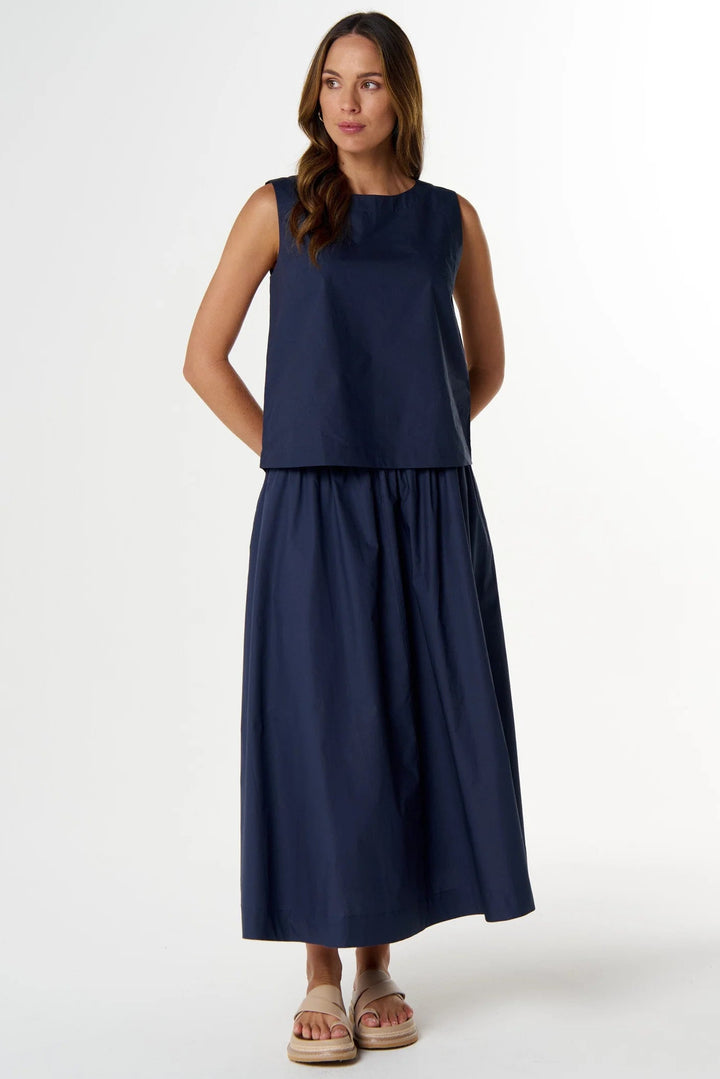 A woman modeling a sleeveless navy blue maxi dress with a cropped top and a flowing skirt, standing against a plain white studio background.