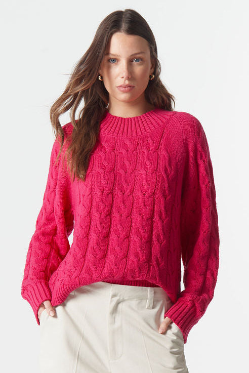 Woman wearing a bright pink sweater and white pants on a white background