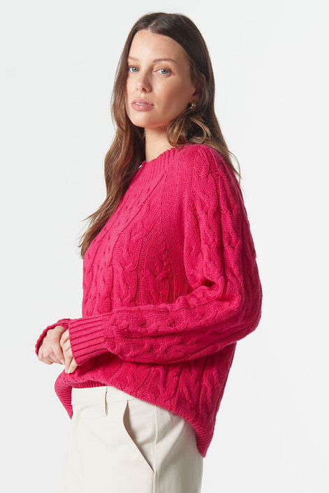 Woman wearing a bright pink sweater and beige pants on a white background