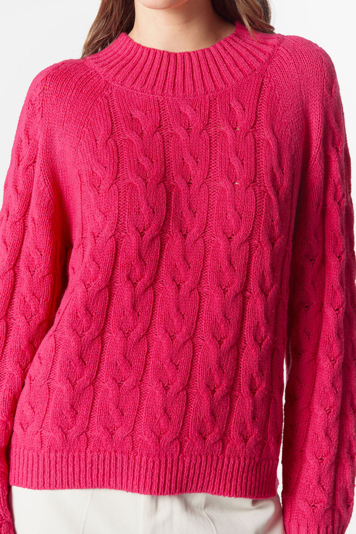 Close-up of a pink cable knit sweater on a plain background