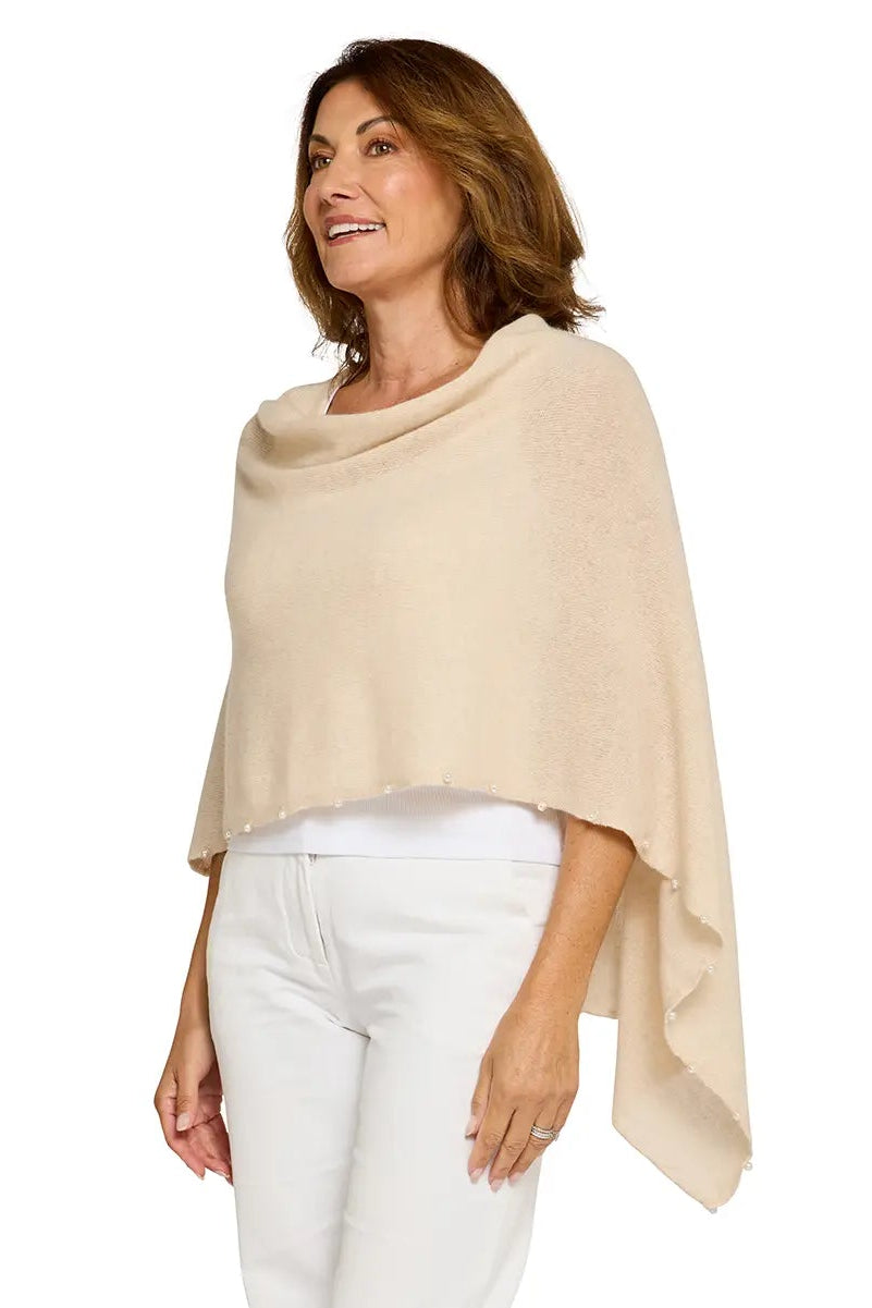 Woman wearing a beige poncho and white pants on a white background
